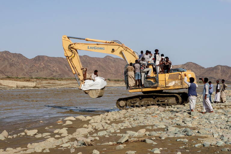 Aid and people are transported on an excavator following devastating floods, in Port Sudan